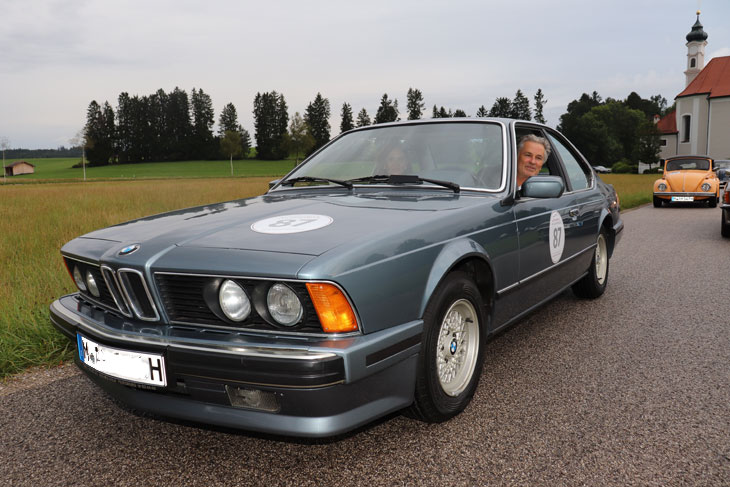 Timothy Peach, unterwegs mit iseiner Tochter beim Zwischenstop mit ihrem BMW 635 CSi Coupé BJ 1987 von „Automobile Meilensteine“ vor der Wallfahrtskirche St. Leonhard in Dietramszell (©Foto. Martin Schmitz)